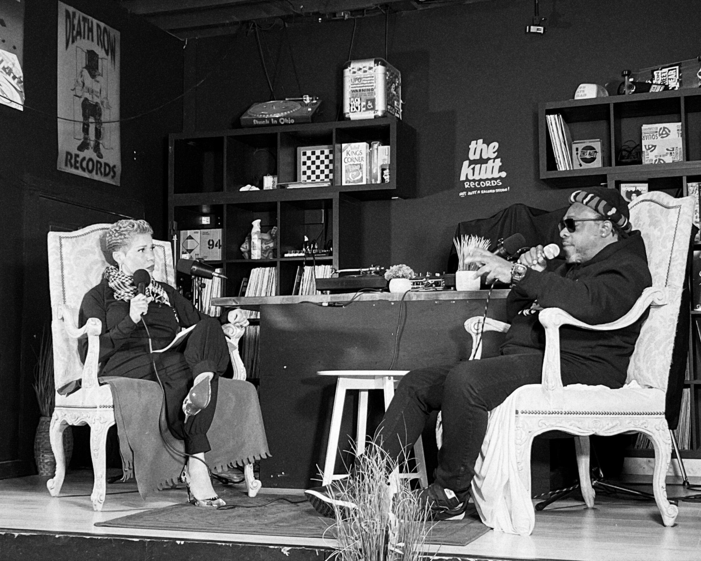 Two people seated in armchairs recording a live podcast conversation